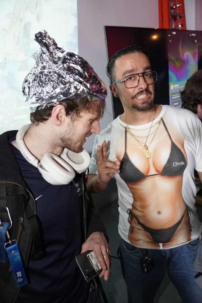 Two attendees: tin foil hat and headphones; shirt graphic referencing Grok.