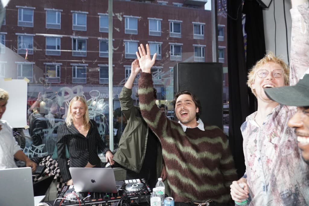 Crowd at the DJ setup, hands in the air, laptop and mixer in frame.